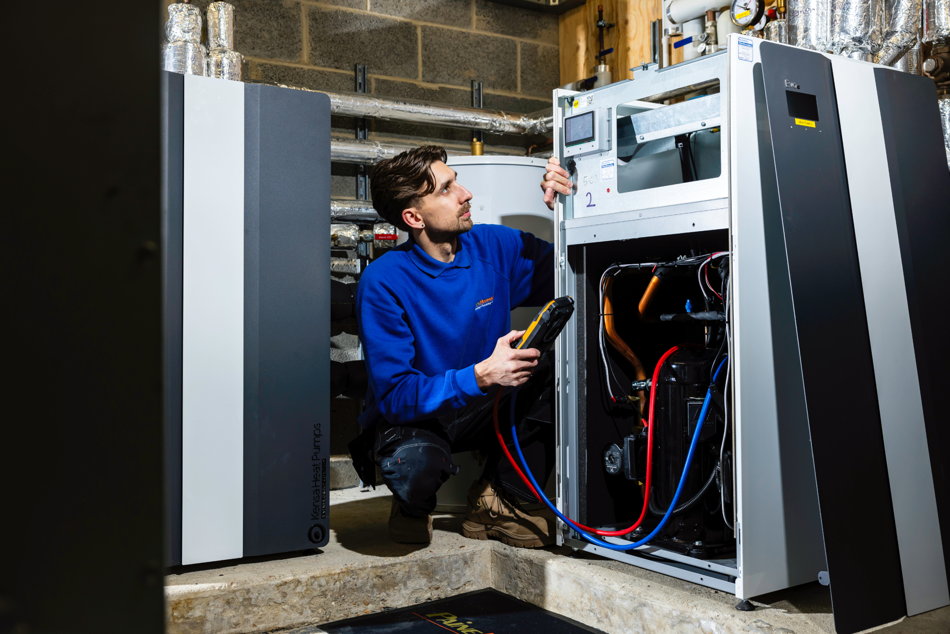 Engineer checking a ground source heat pump unit in a plant room during installation or servicing.