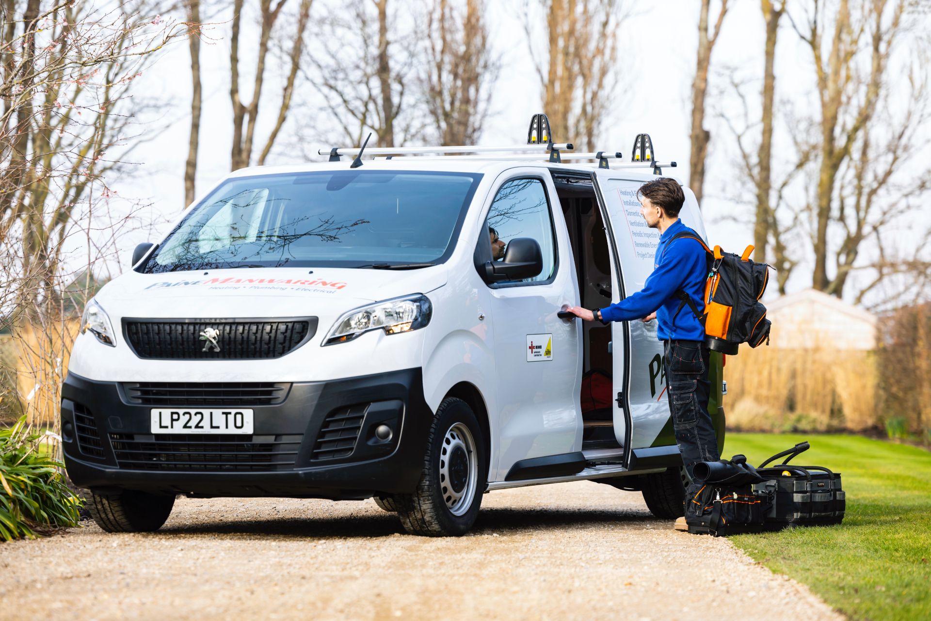 Engineer standing beside a Paine Manwaring service van, preparing equipment for a heating installation on a residential driveway.