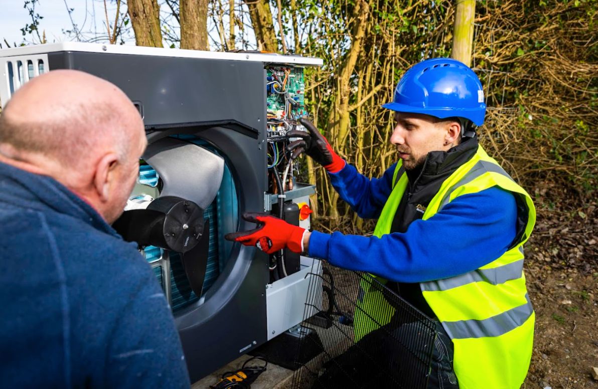 Engineer showing and inspecting the internal components of an air source heat pump unit while speaking with a customer.